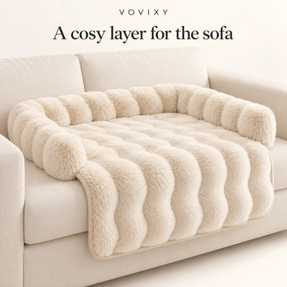 Beige plush dog sofa mat with raised back and side bolsters on a light sofa